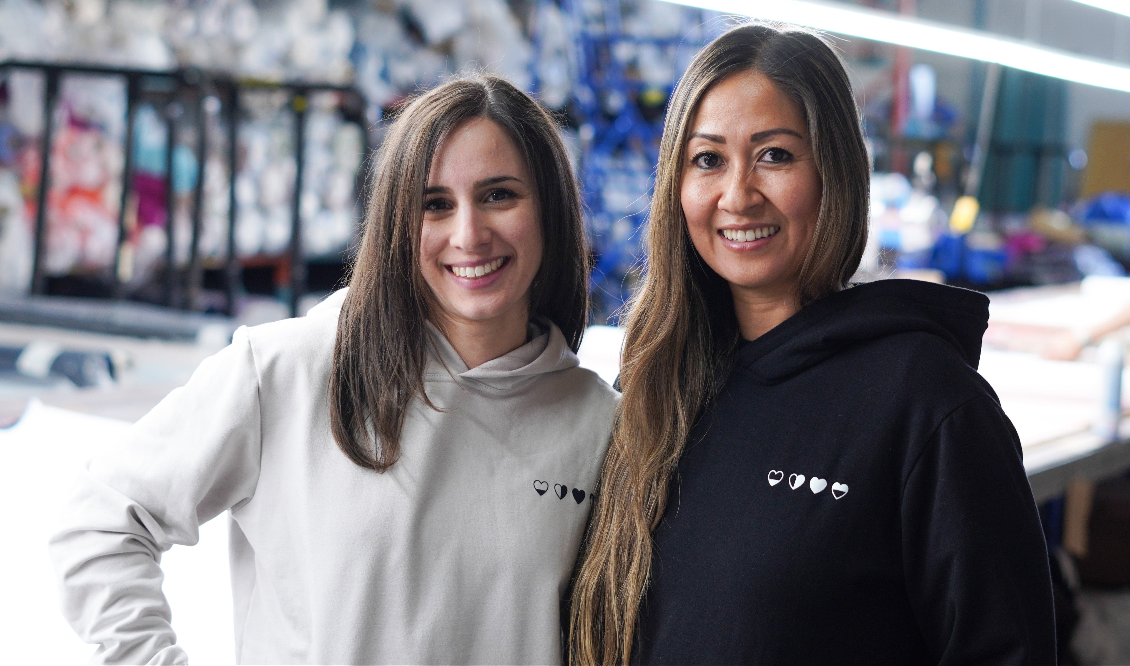 HeartWear Co. founders standing in a Canadian garment factory, creating sustainable fashion with ethical values.