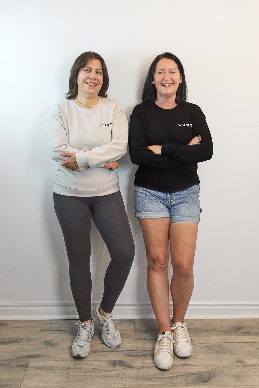 Two women in stone and black Heart Sweaters—meaningful, comfortable apparel for everyday self-care.