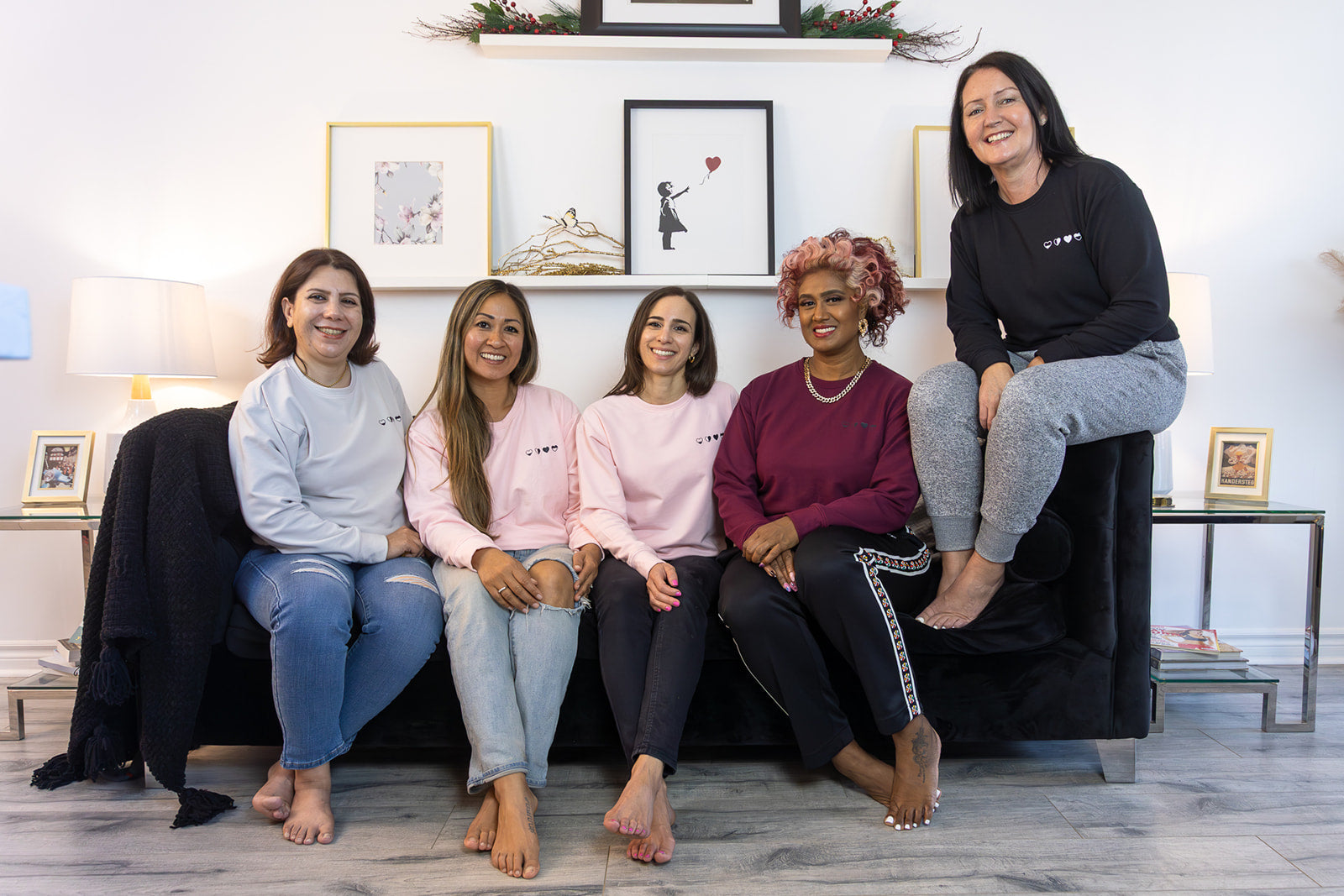 Five women sitting on a couch wearing HeartWear Co. comfort clothing, representing community, healing, and emotional support.