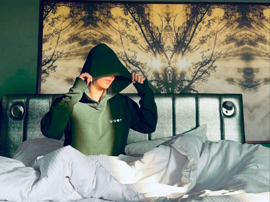 Person wearing a green hoodie in bed with a tree mural in the background