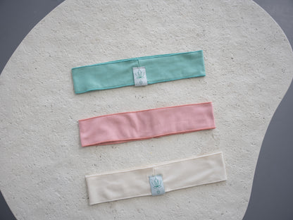 Three bamboo cotton headbands in pink, natural, and pistachio from HeartWear Co.’s Love Collection, laid flat side by side