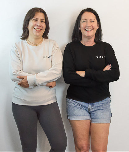 Two women in stone and black Heart Sweaters—meaningful, comfortable apparel for everyday self-care.
